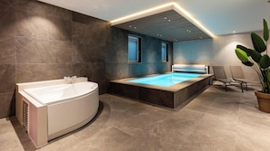 A modern bathroom with a freestanding bathtub, a large rectangular pool, and a seating area with chairs.
