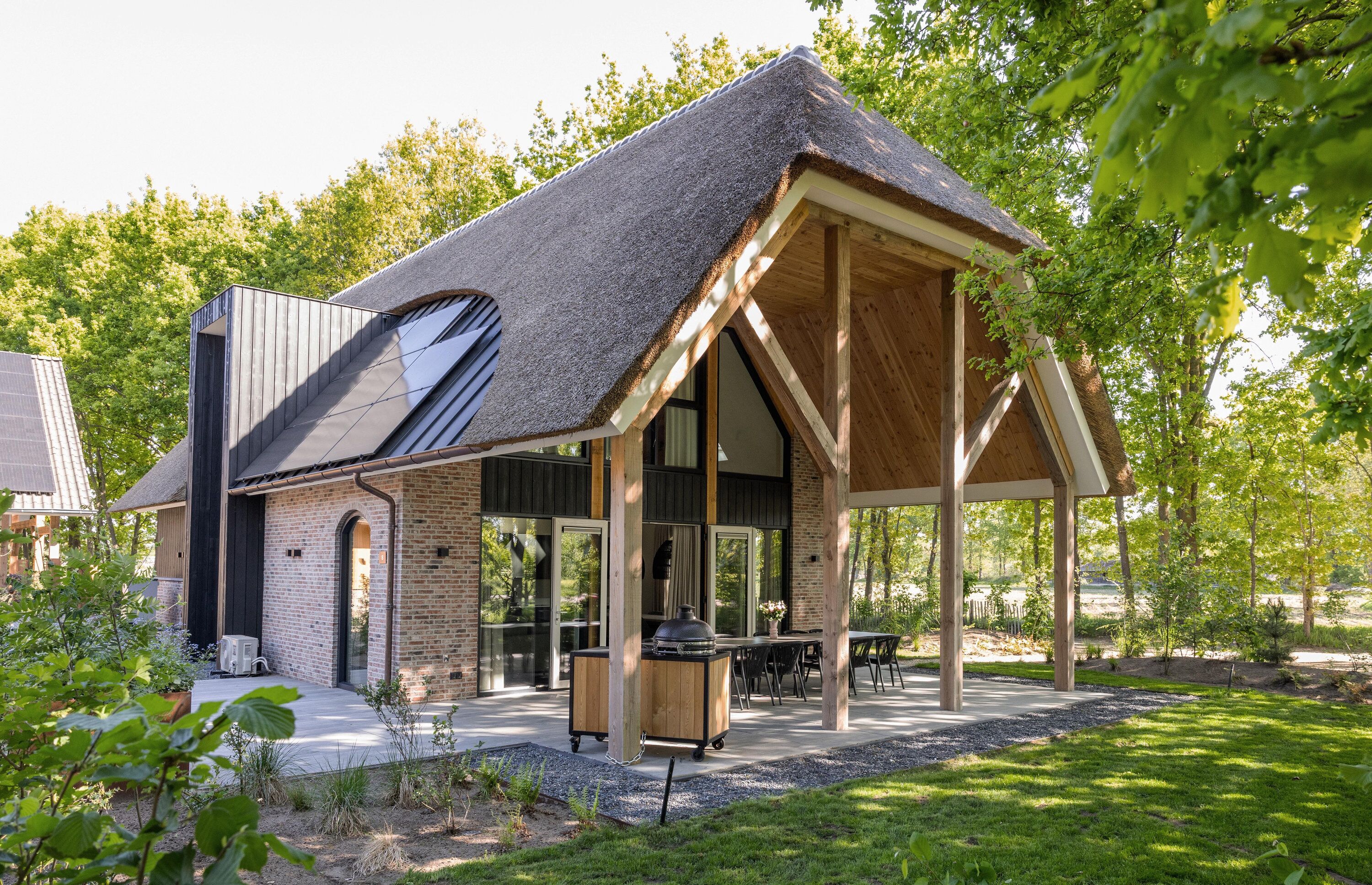 A modern house with a thatched roof, brick walls, and a covered outdoor area with a grill.