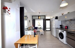 Eine moderne Küche mit Waschmaschine, eine Essecke mit Tisch und Stühlen sowie ein Wohnbereich mit Sofa und Fenster.