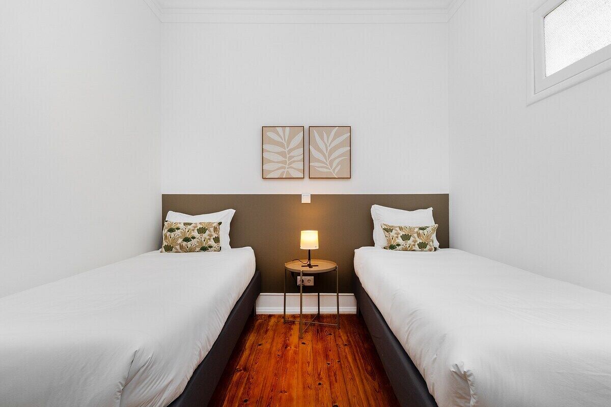 Une chambre d’hôtel avec deux lits, une petite table de chevet avec une lampe et deux œuvres d’art accrochées au mur.