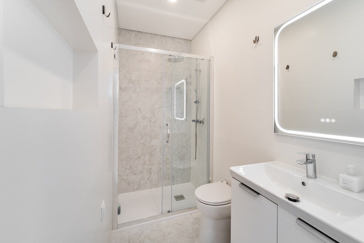 A modern bathroom with a glass-enclosed shower, a white toilet, and a large mirror above the sink.