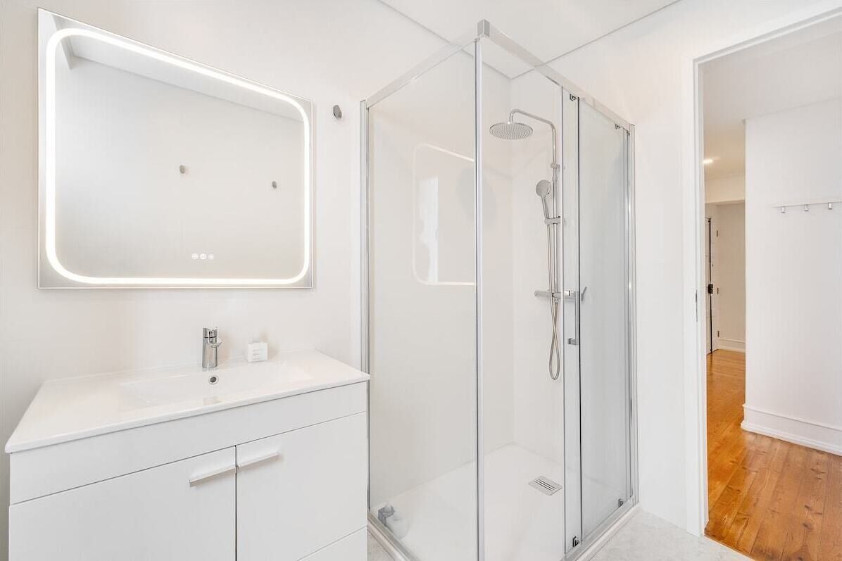 A modern bathroom with a glass-enclosed shower, a white vanity with a mirror, and a recessed light.