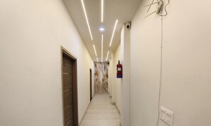 A narrow hallway with a wooden door, a fire extinguisher, and a ceiling with linear lighting. - Hotel Imperial Panipat (Panipat)