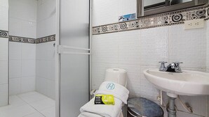 Ein Badezimmer mit Dusche, Toilettenpapier, Waschbecken und Mülleimer.