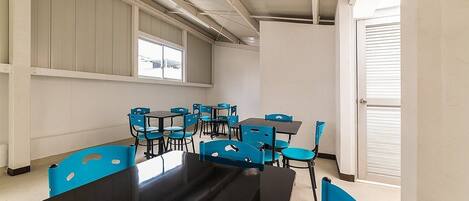 Un salón de conferencias con una mesa larga y sillas azules, ventanas amplias y una puerta con persianas.
