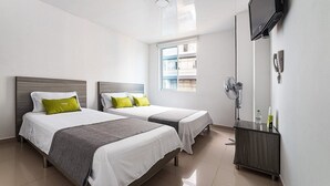 Ein Hotelzimmer mit zwei Betten, einem Fernseher, einem Spiegel und einem Fenster mit Blick auf Gebäude.