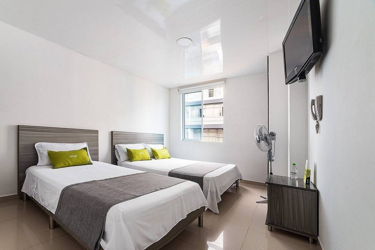 A hotel room with two beds, a TV, a mirror, and a window with a view of buildings.