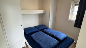 Una habitación pequeña con cama, luz en el techo, ventana y puerta.