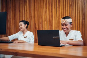 Two individuals seated at a wooden table with laptops, in a room with vertical wooden paneling. - Candidasa Hills (Bali)