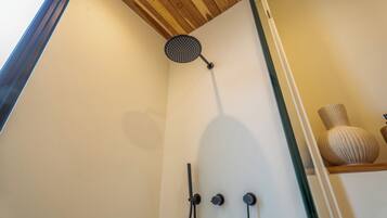 Een douche met een regendouchekop en twee knoppen, waarschijnlijk voor temperatuur en waterdruk, in een ruimte met een houten plafond en een witte wand.