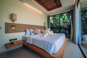 Una habitación de hotel moderna con una cama grande, cabecera de madera, mesita de noche con frutero y vistas a exuberante vegetación a través de amplias ventanas.