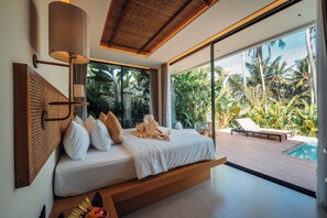 A modern bedroom with a bed, a bedside lamp, a view of a pool, and tropical plants. - Candidasa Hills (Bali)