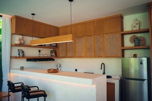A modern kitchen with wooden cabinets, a central island, and a built-in refrigerator. - Candidasa Hills (Bali)