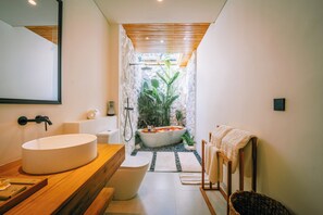A modern bathroom with a large oval sink, a freestanding toilet, a bathtub, and a wooden vanity. - Candidasa Hills (Bali)