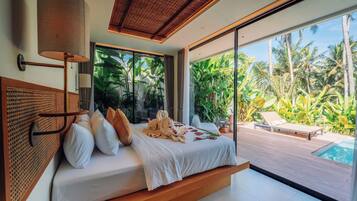 A modern bedroom with a large bed, a view of a swimming pool, and tropical plants.