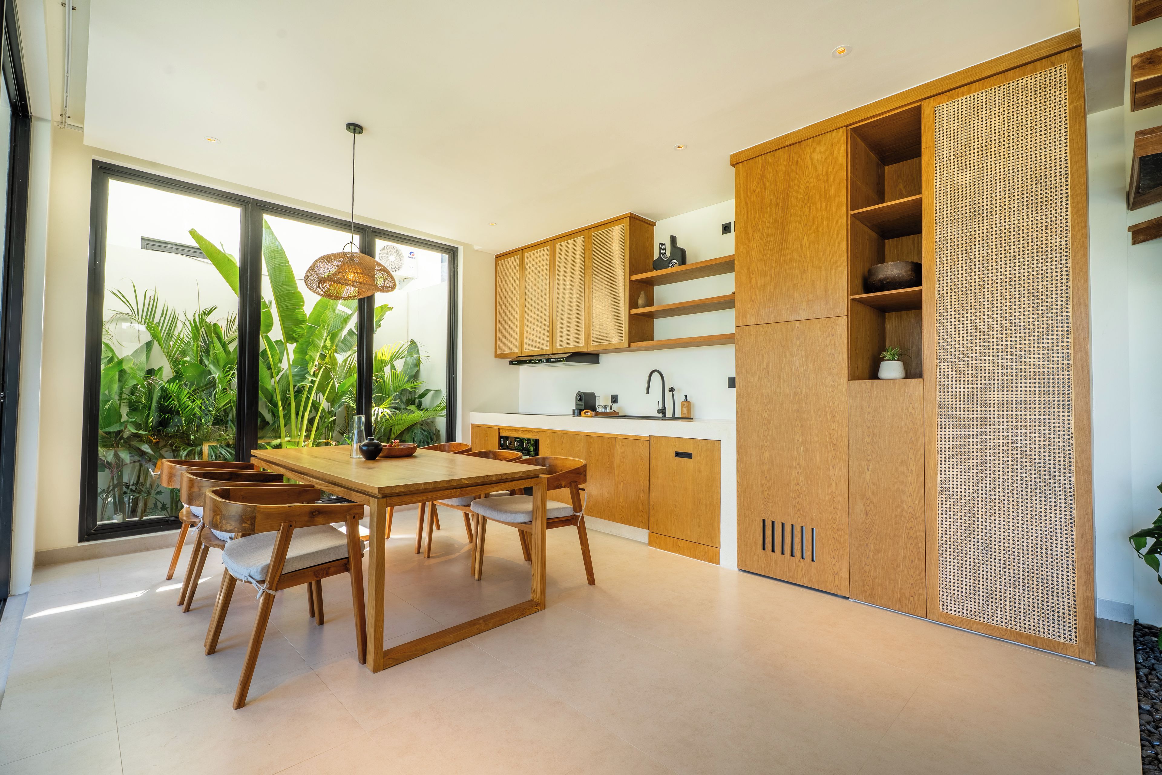 Een moderne keuken met houten kasten, een eettafel met stoelen en een groot raam met planten.
