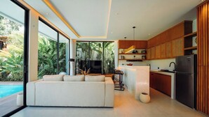 Cocina moderna con armarios de madera, un refrigerador negro y una zona de comedor con mesa y sillas blancas.