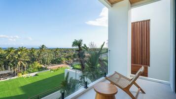 A balcony with a view of a green lawn and palm trees, a wooden chair, and a small round table.