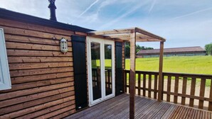 Eine Holzterrasse mit einer Glastür, die zu einem überdachten Außenbereich führt.