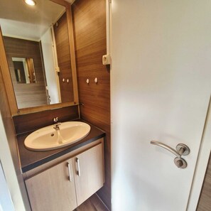 A bathroom with a sink, mirror, and wooden cabinets. - And why not?...rent a mobile home in the heart of nature (Ramonchamp)