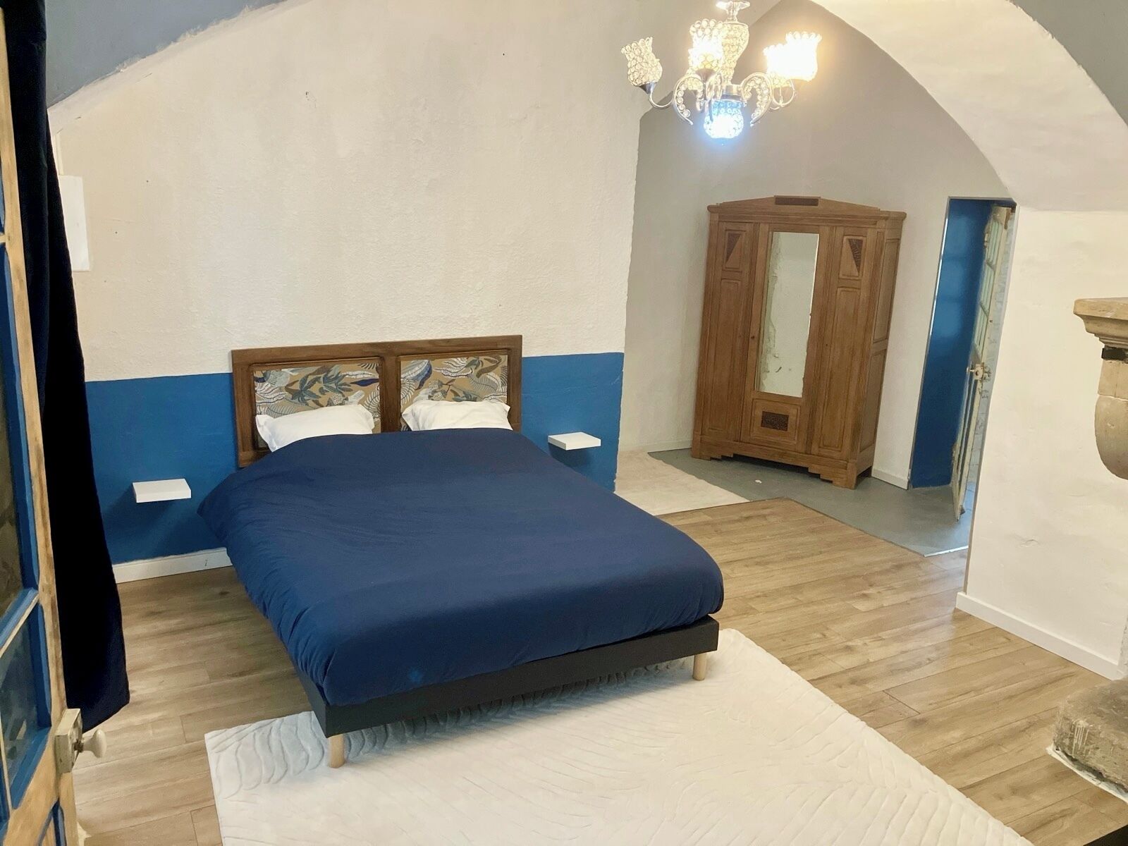 Een slaapkamer met een bed, een houten garderobe en een kroonluchter.