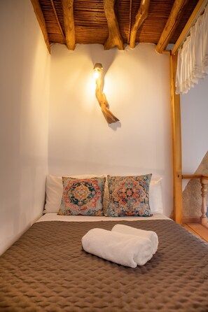Ein Schlafzimmer mit einem Bett, zwei Kissen, einem weißen Handtuch, Holzbalken und einer Wandleuchte.