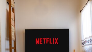 Ett rum med en platt-TV som är monterad på väggen och som visar ordet ”NETFLIX” med röda bokstäver.