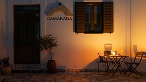 A building with a sign reading 'CAMARADA,' a potted plant, a table with chairs, and a bottle of wine.