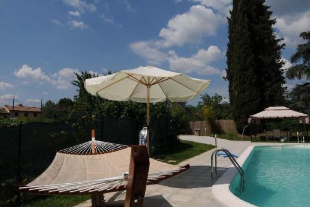 Ein Schwimmbecken mit Holzterrasse, einer Hängematte und einem weißen Sonnenschirm.