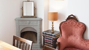 Una habitación con chimenea, espejo, lámpara, sillón y una pila de libros.