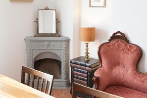 Une pièce avec une cheminée, un miroir, une lampe, une chaise et une pile de livres.