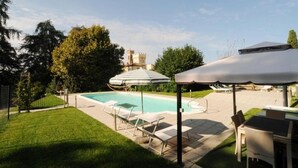 Zona de piscina con sillones de descanso, sombrillas y un castillo al fondo.
