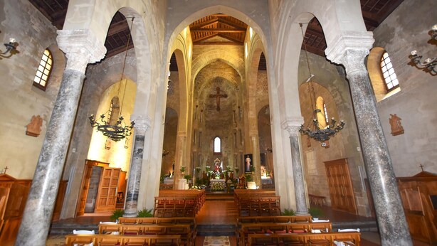 Interior de iglesia con altos techos abovedados, bancos de madera y un altar central.