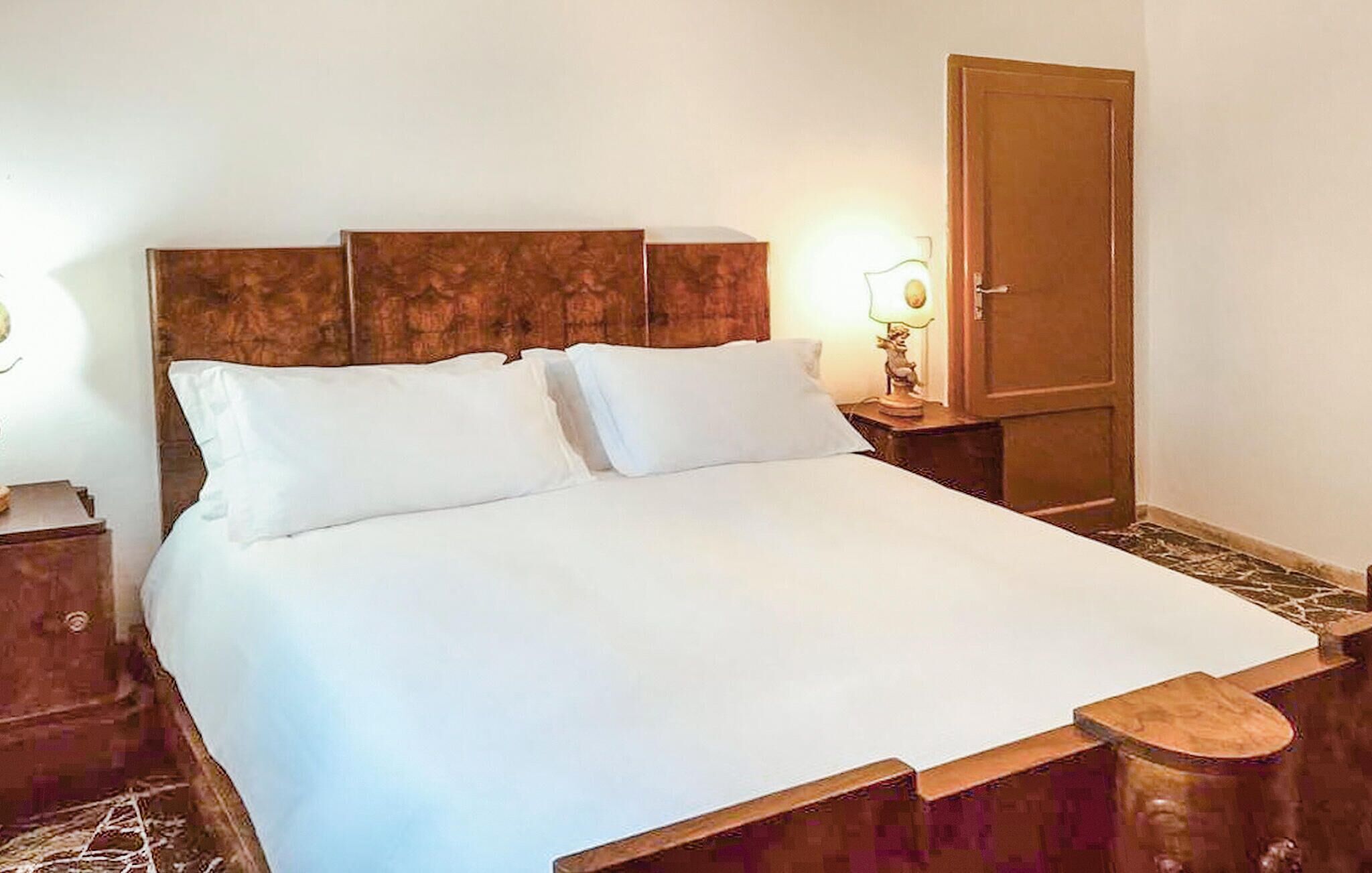 A bed with a wooden headboard, two pillows, a nightstand with a lamp, and a wooden wardrobe.