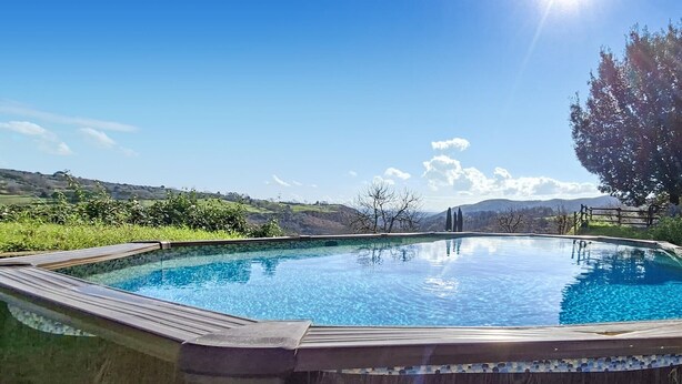 A rectangular pool with a wooden deck, surrounded by greenery and hills in the background. - Amazing home in Manciano with private swimming pool, can be inside or outside (Manciano)