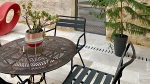 An outdoor seating area with a round metal table and two chairs, a red circular object, and potted plants.