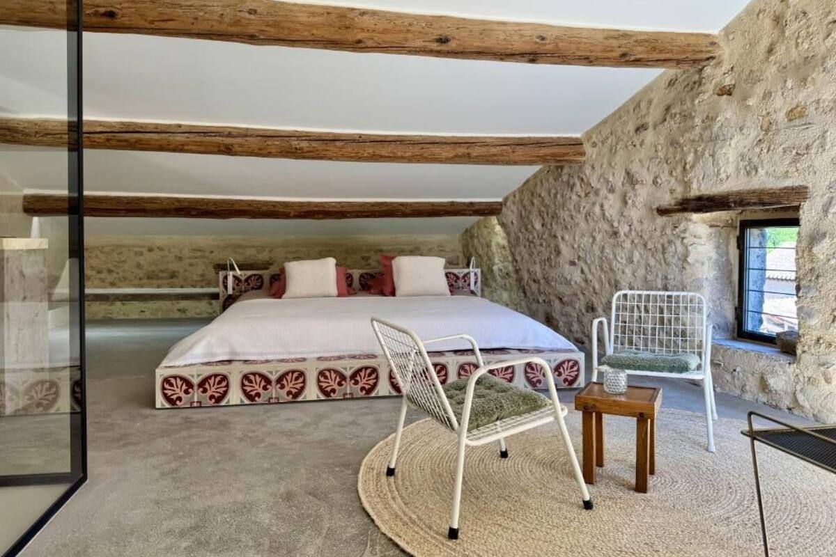 Ein Schlafzimmer mit Bett, Stuhl, kleinem Tisch und einer Steinwand.