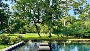 A tranquil outdoor pool area with a stone pathway leading into the water, surrounded by lush greenery.