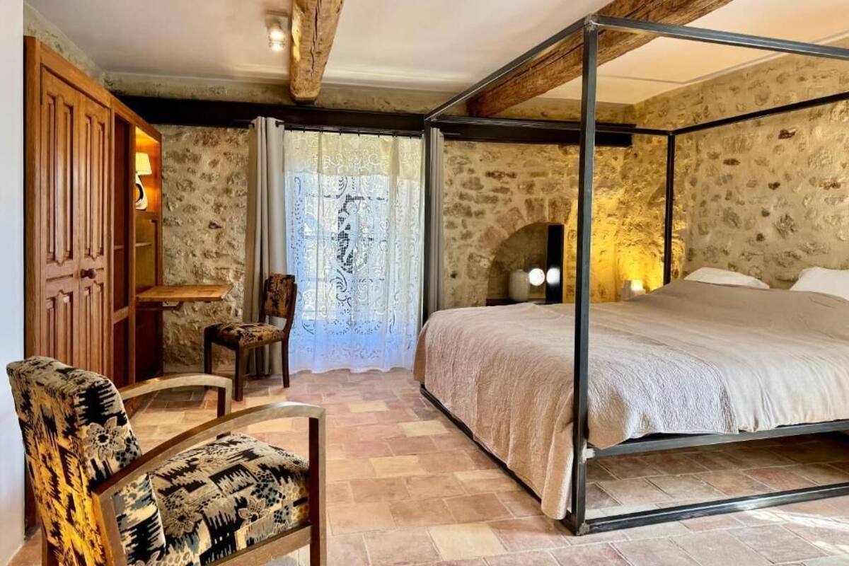 Ein Schlafzimmer mit Himmelbett, einem Holzstuhl, einem kleinen Tisch und einer Steinwand.
