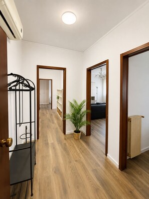 Ein Korridor mit Holzboden, einem Heizkörper, einem Blumentopf und einem schwarzen Metallregal.