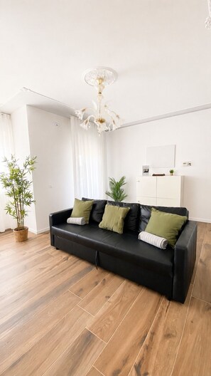 Ein modernes Wohnzimmer mit einer schwarzen Ledersofa, Holzböden, einer weißen Decke und einem Kronleuchter.