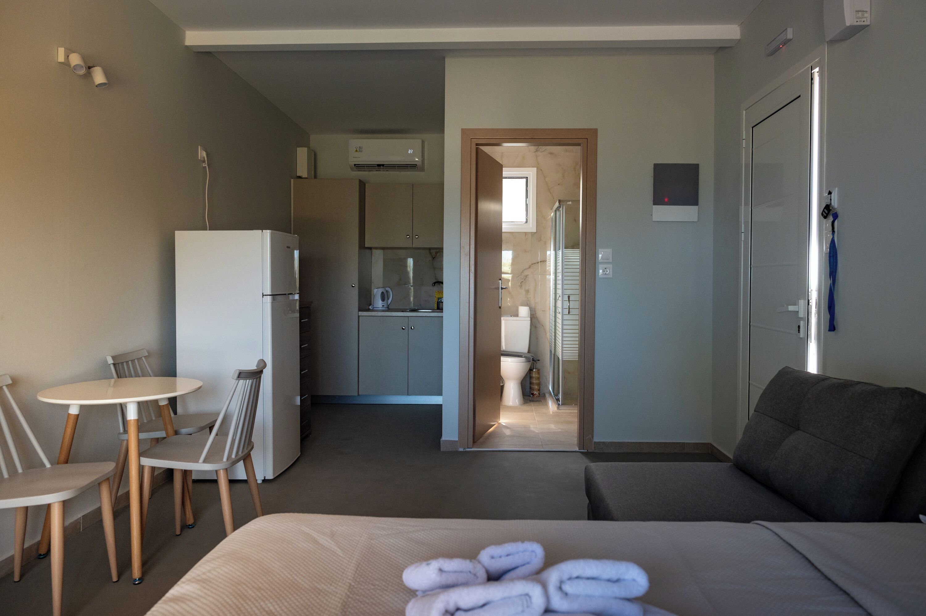 A hotel room with a bed, a small dining table with chairs, a kitchenette, and a bathroom visible through an open door.