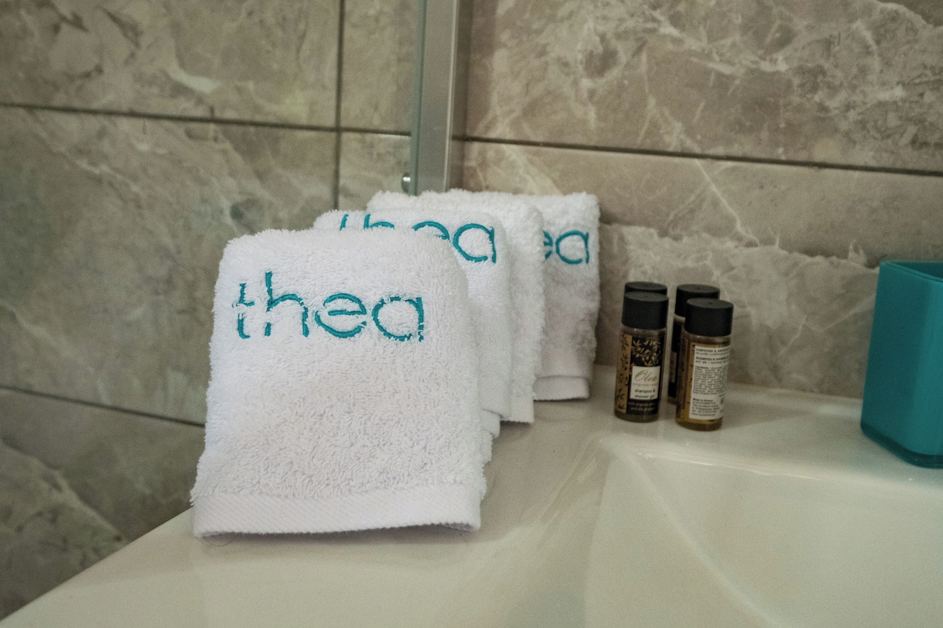 A bathroom with white towels stacked on a counter, a teal soap dispenser, and two bottles of toiletries.