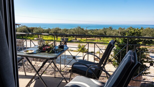 A balcony with a table and chairs, overlooking a coastal landscape. - Thea Luxury Residences (Zacharo)