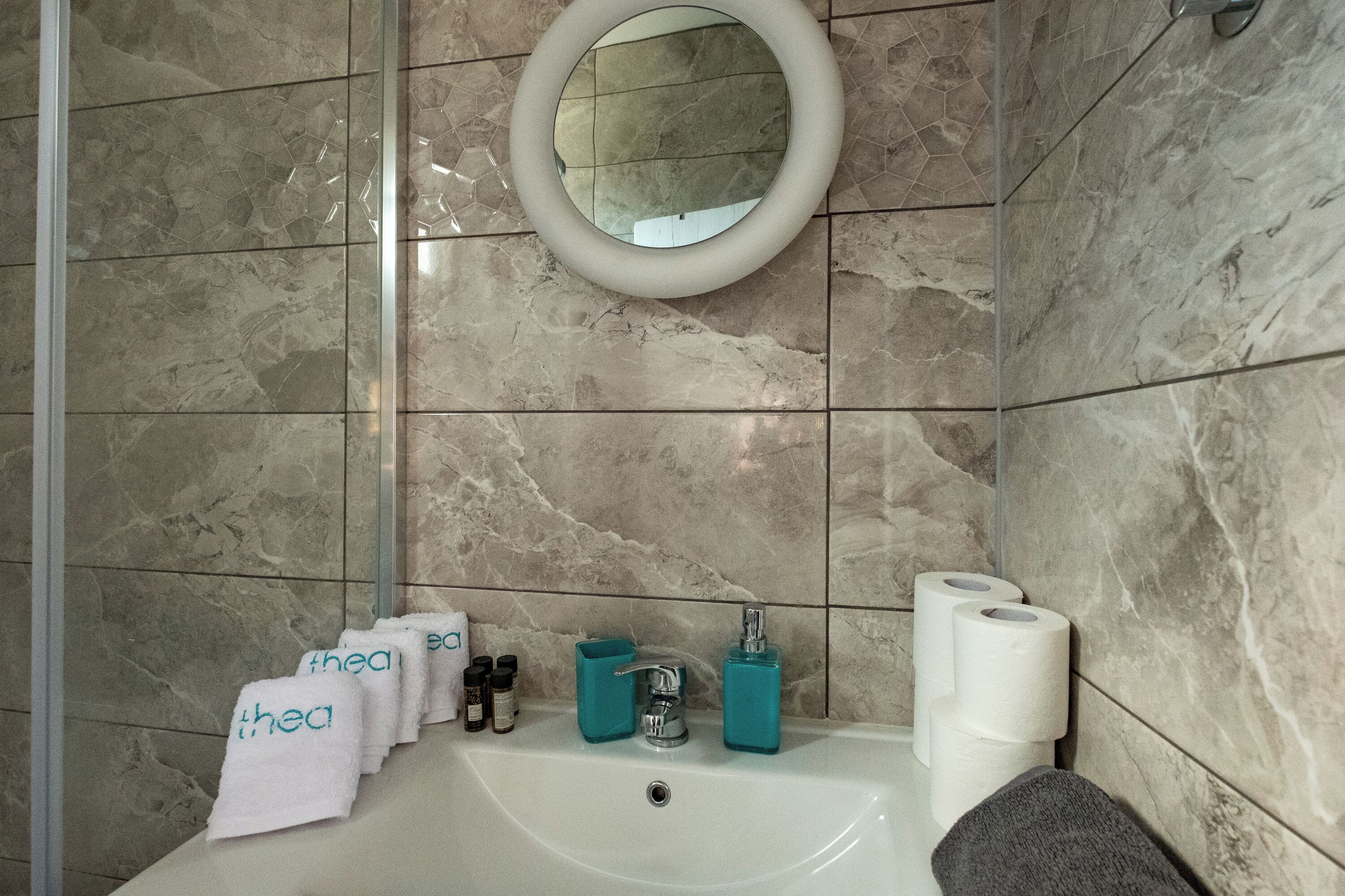 Un baño con lavamanos, espejo, artículos de aseo y toallas.