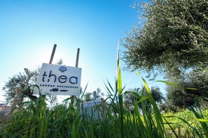 A sign with the word 'thea' partially visible, surrounded by greenery and trees. - Thea Luxury Residences (Zacharo)