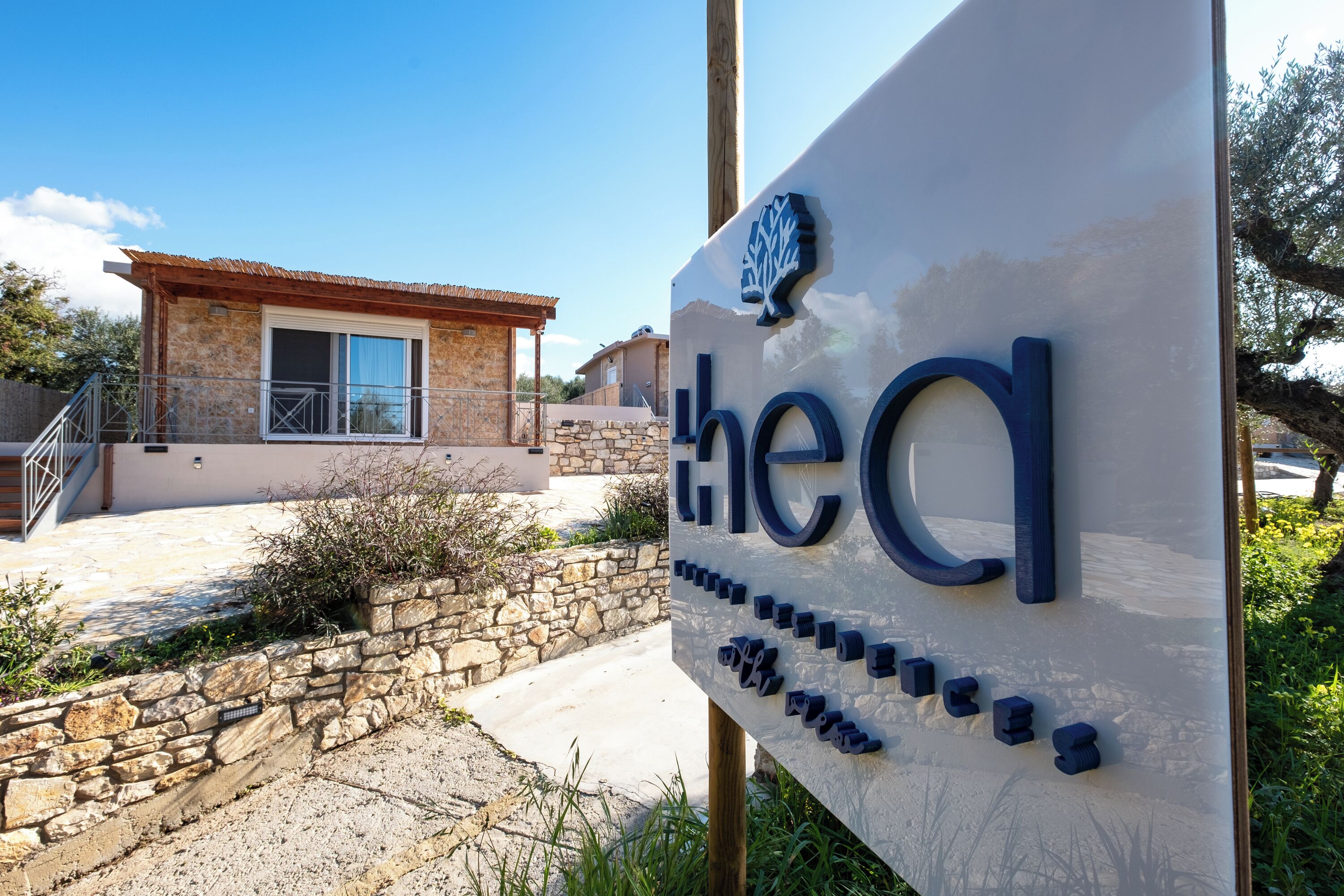 A sign with the name 'thecl' and a stone wall with a staircase leading to a building with a tiled roof.