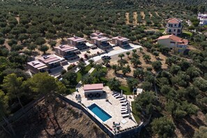 An aerial view of a residential area with multiple houses, a swimming pool, and a landscaped garden. - Thea Luxury Residences (Zacharo)
