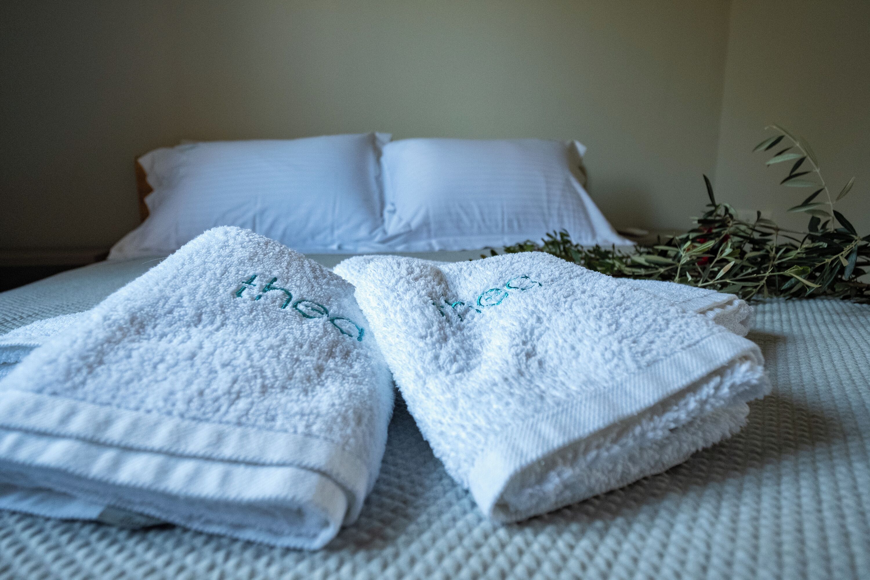 A neatly made bed with white linens and two folded towels with embroidered text.
