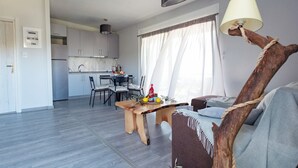 A modern kitchen with grey cabinets, a dining area with a wooden table, and a living room with a sofa and a lamp. - Thea Luxury Residences (Zacharo)
